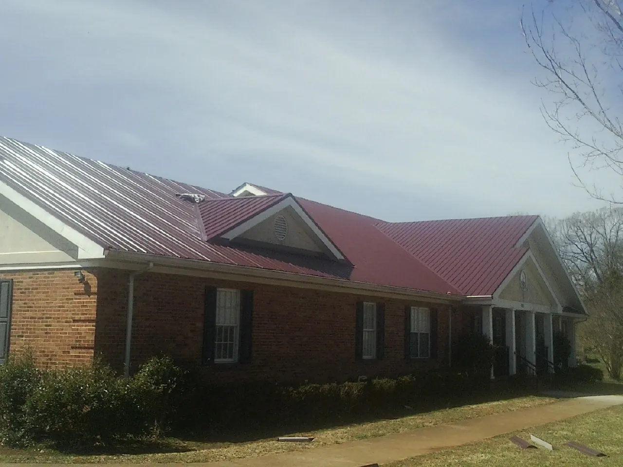 Red metal roof with gabled entries on a long brick building, from a Hail Damage Roof Repair job in Brevard