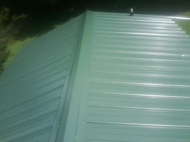 New green metal panels meeting at the ridge of a roof — Flat Roof Repair work by our crew in Brevard