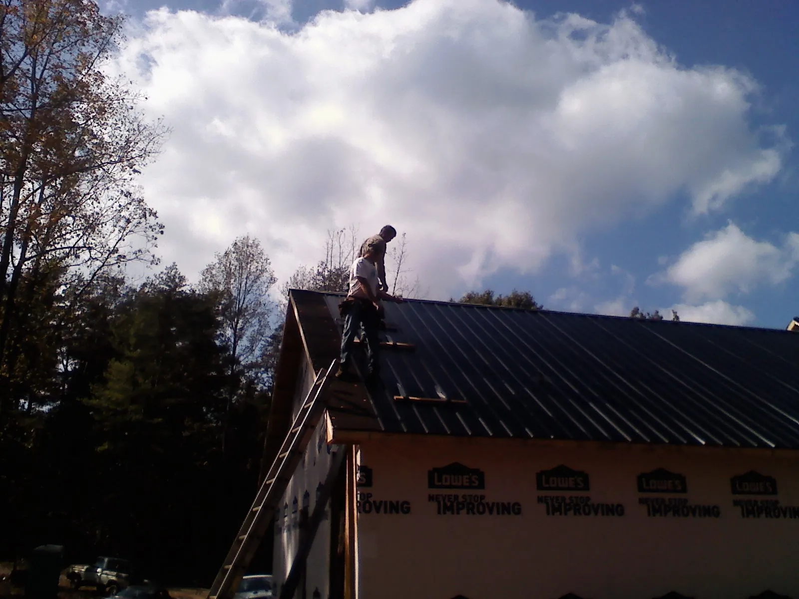 Roofer fastening dark metal panels high against a cloudy sky, from a Roof Inspection job in Brevard